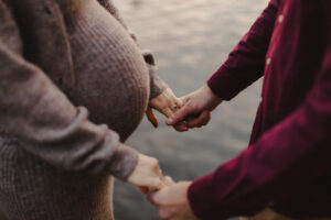 Couple maternity Photos in Autumn in London. This is a close-up photo of a couple holding hands in front of a lake, you see the mother's baby bump.