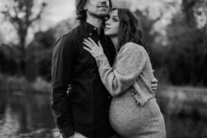 Couple maternity Photos in Autumn in London. This is a black and white photo of a couple embracing, they are standing in front of a lake.